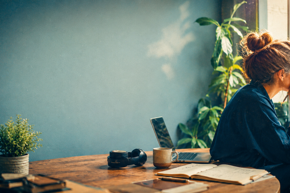 Editorial header image showing a marketer sitting at a desk by a window, reflecting beside a laptop, notebook, headphones, and coffee, used for an article about deep work and staying strategic in an AI-saturated workplace.